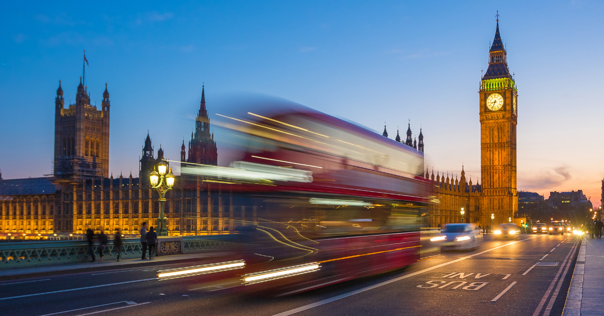 Iconic Double Decker bus on the move on Westminster bridge with illuminated Big Ben clock tower and Parliament at background at blue hour